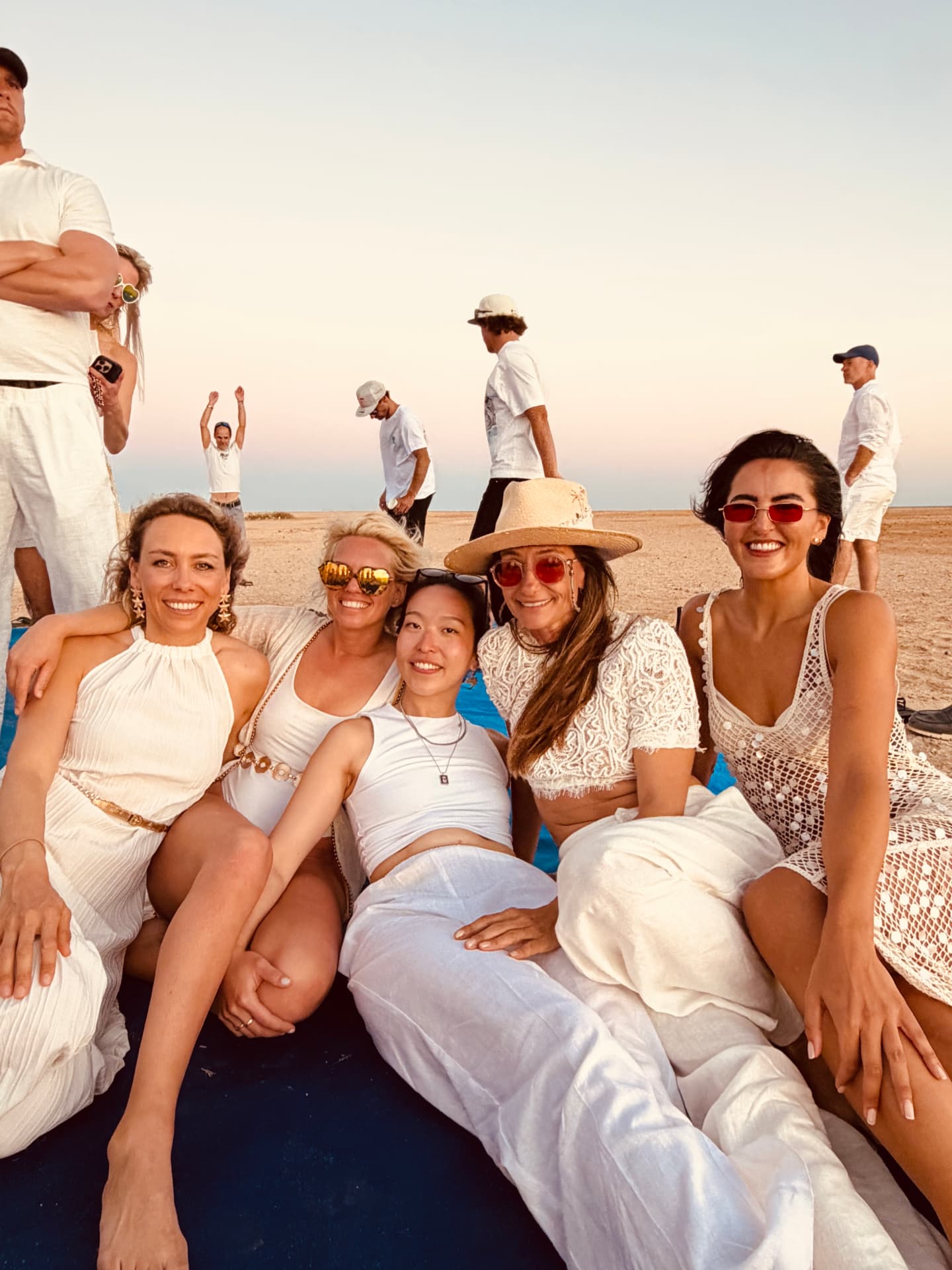 Group of friends dressed in white relaxing together at a beach sunset party