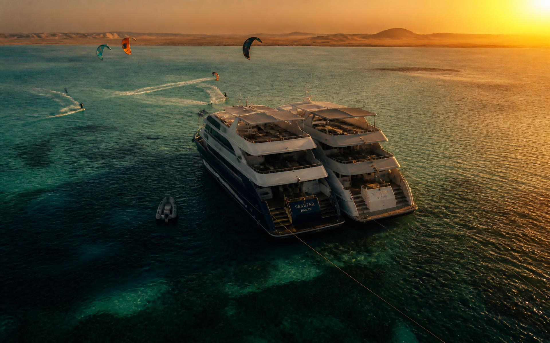 Two luxury yachts anchored in a turquoise Red Sea lagoon at sunset with kitesurfers riding nearby