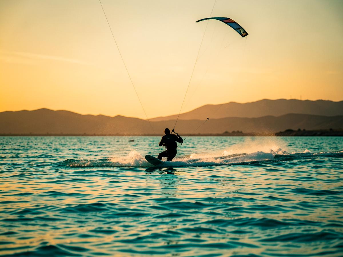 Kitesurfer riding flat turquoise lagoon water at sunset